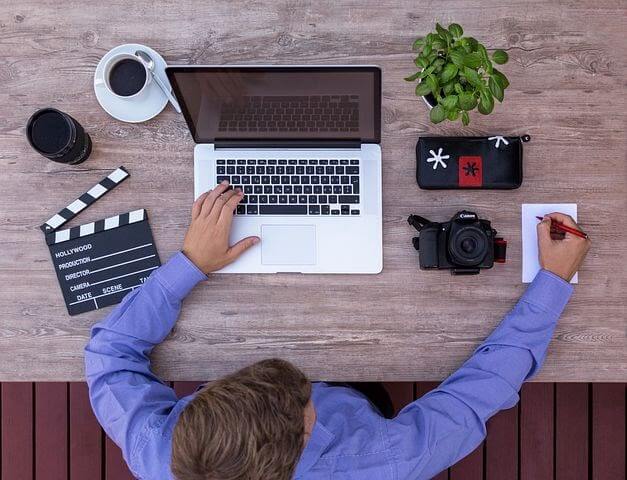 A filmmaker working on laptop with his camera and coffee on the table.